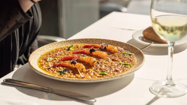 Risotto cremoso con azafrán, camarones a la parrilla, pimientos rojos y hierbas frescas, acompañado de pan tostado.