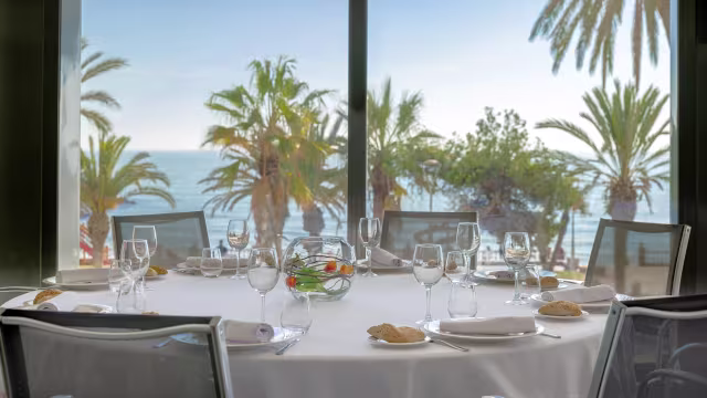 Mesa elegantemente dispuesta con vista al océano, decorada con frutas frescas y panecillos dorados, sugiriendo una experiencia gastronómica sofisticada.