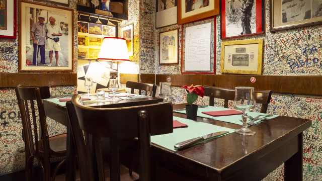 Interno accogliente di un ristorante con tavolo in legno, tovagliette verde menta e decorazioni murali eclettiche.