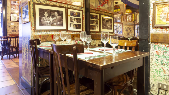 Interno accogliente con tavolo in legno per sei, decorato con fotografie in bianco e nero e memorabilia colorati, creando un'atmosfera nostalgica.