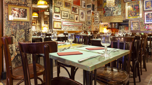 Interno accogliente di un ristorante con opere d'arte e fotografie, sedie in legno e illuminazione calda.