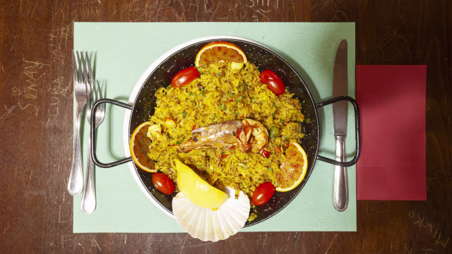 Paella colorata con riso allo zafferano, gamberi, scallop, arance e pomodorini.