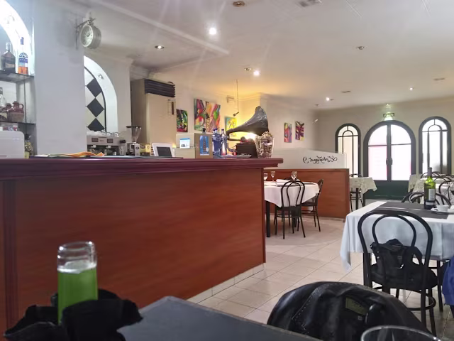 Interior de restaurante luminoso y acogedor, con barra de madera pulida, arte colorido en las paredes y mesas con manteles blancos.
