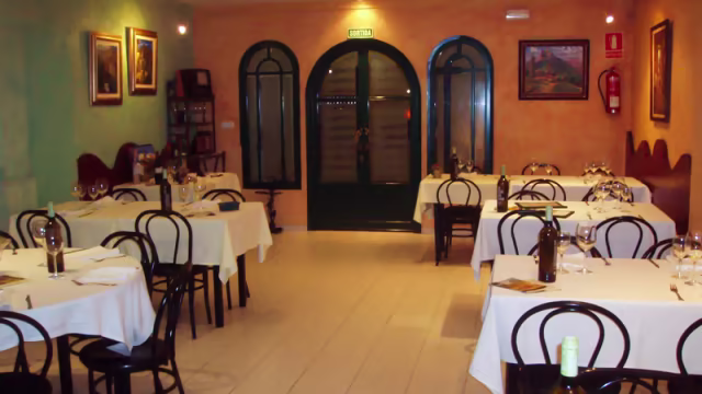 Interior de un restaurante acogedor con mesas vestidas con manteles blancos, iluminación cálida y decoración en tonos suaves.