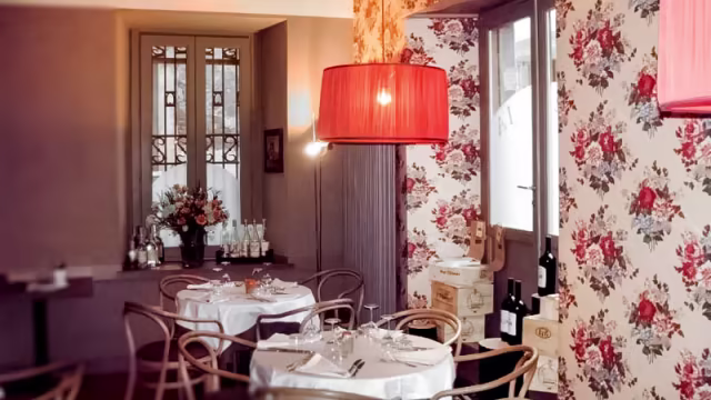 Interno di un ristorante accogliente con carta da parati floreale e un'atmosfera calda, illuminato da una grande lampada a sospensione rossa.