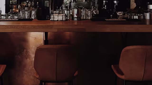 Gezellige bar met een warme sfeer, houten barblad, aardse decoratie, comfortabele leren stoelen en sfeervolle verlichting, perfect voor drankjes en socializen.