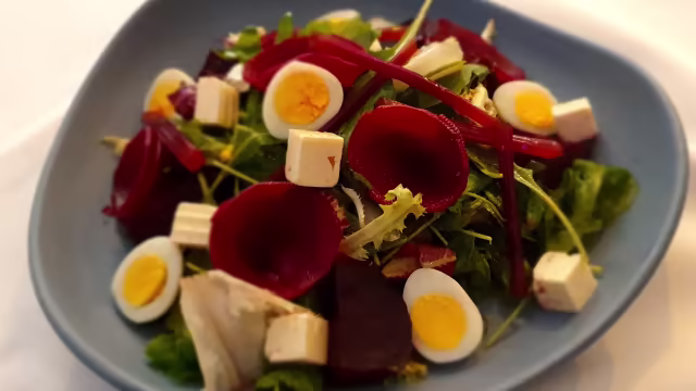 Ensalada fresca con mezcla de hojas verdes, remolachas asadas, huevos de codorniz, queso en cubos y tiras de pimiento rojo.