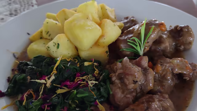 Carne brasata in salsa ricca, accompagnata da patate arrosto e verdure saltate con fiori edibili.