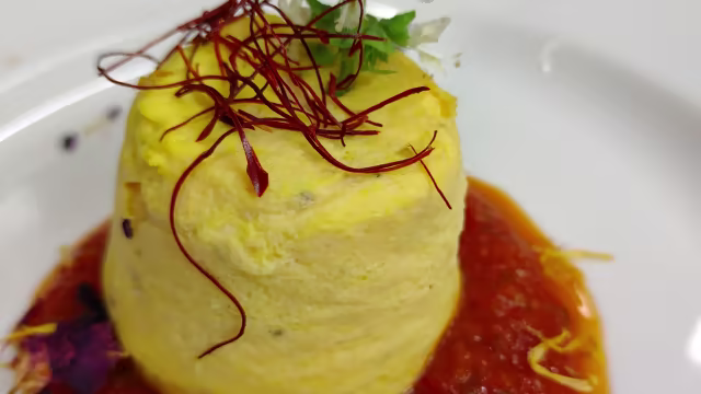 Purè di patate cremose con zafferano, servito con salsa rossa e decorato con fiori edibili e erbe fresche.