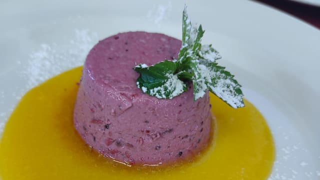 Mousse cremosa ai frutti di bosco, guarnita con foglia di menta e coulis di frutta gialla.