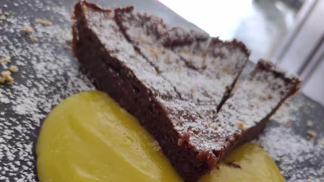 Dessert al cioccolato ricco, servito con una salsa cremosa gialla, che offre un equilibrio di sapori.