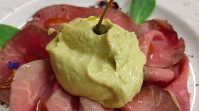 Carpaccio di manzo con salsa cremosa verde e guarnizione di erbe fresche.