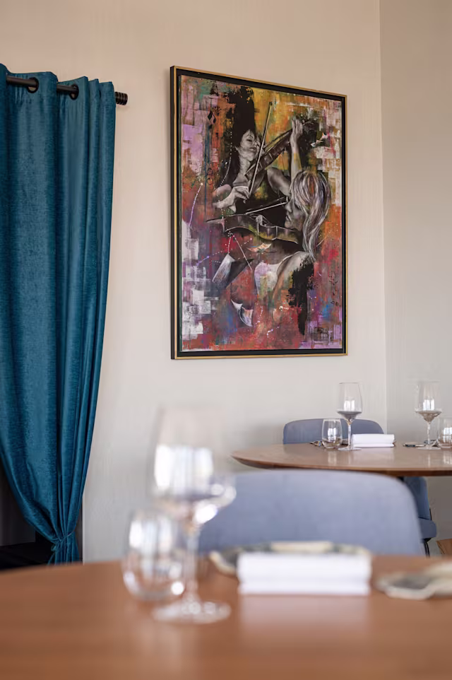 Intérieur de restaurant élégant avec une décoration moderne, des murs ornés d'une peinture abstraite colorée et des rideaux bleus encadrant une fenêtre, créant une atmosphère sophistiquée et confortable.
