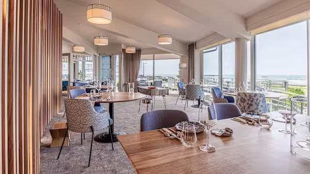 Intérieur de restaurant moderne avec de grandes fenêtres, offrant une ambiance lumineuse et accueillante, mêlant sièges élégants et tables en bois.