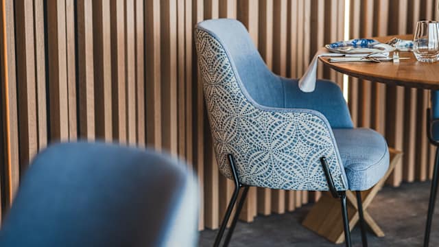 Intérieur de restaurant moderne avec une chaise élégante à deux tons, en tissu bleu doux et dossier texturé, entouré de panneaux en bois créant une atmosphère chaleureuse.