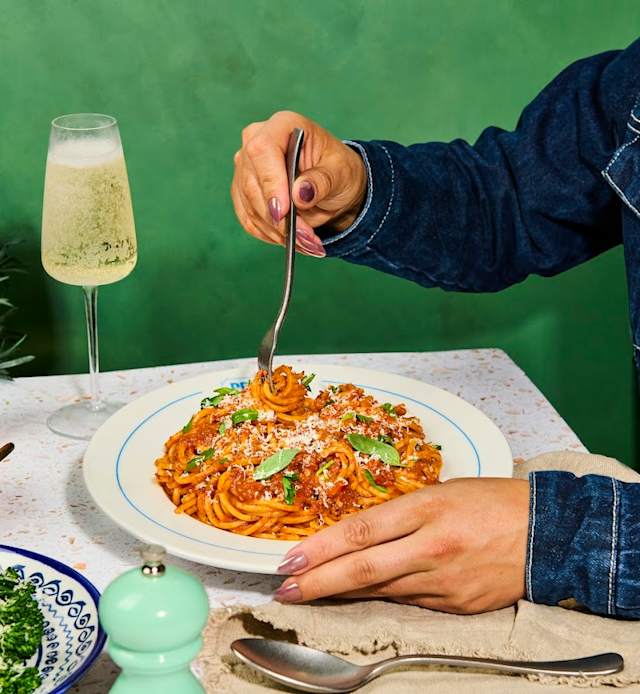 Spaghetti topped with rich tomato sauce, garnished with fresh basil and grated cheese, served with a glass of sparkling beverage.