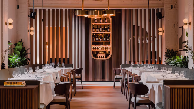 Interni moderni ed eleganti con listelli di legno, illuminazione calda, piante verdi e un bar raffinato.