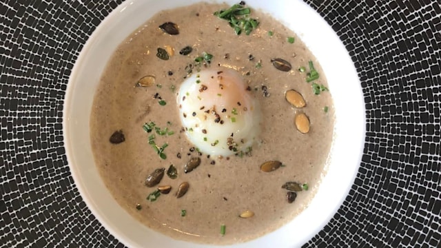 Soupe crémeuse à la texture lisse, à base de noix ou de graines, garnie d'un œuf poché, de graines de courge toastées et d'herbes finement hachées.