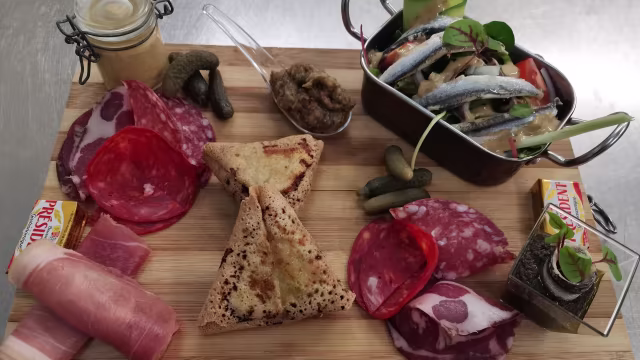 Plateau de charcuterie avec une sélection de viandes séchées, crêpe dorée, cornichons, moutarde et légumes marinés, offrant une variété de saveurs et de textures.