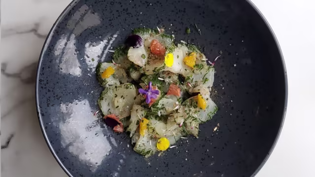 Plat de ceviche de poisson blanc finement découpé, mélangé avec des herbes fraîches et garni de fleurs comestibles et de touches de fruits, offrant une présentation élégante et rafraîchissante.