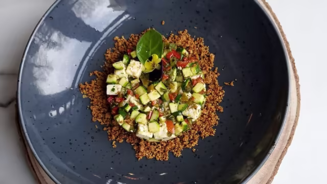 Plat léger et rafraîchissant avec une base croustillante de composants dorés, garnie de légumes frais en dés, dont des courgettes vertes et des tomates rouges, rehaussée d'herbes et d'une feuille de laurier.