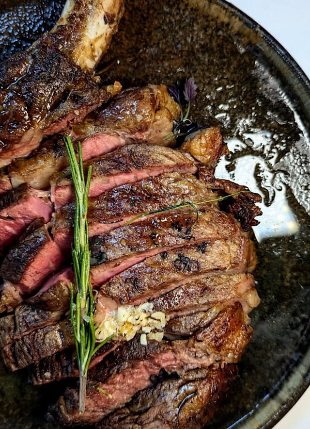 Juicy steak with a savory crust, garnished with fresh rosemary and minced garlic, showcasing its tenderness and quality.