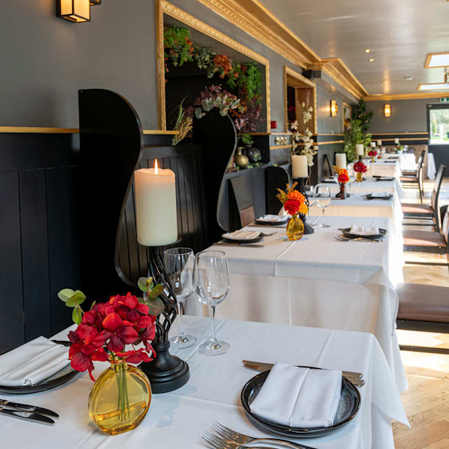 The restaurant interior features neatly arranged tables with white tablecloths and fresh flower vases, complemented by elegant moldings and soft lighting, creating a refined ambiance for special occasions.