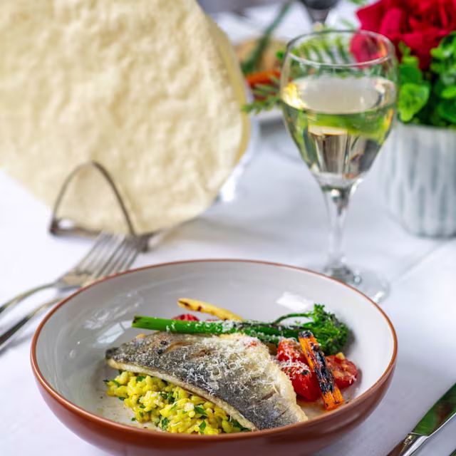 Pan-seared fish fillet with crisp skin, served with creamy herb-infused risotto, roasted cherry tomatoes, and chargrilled asparagus, garnished with grated cheese.