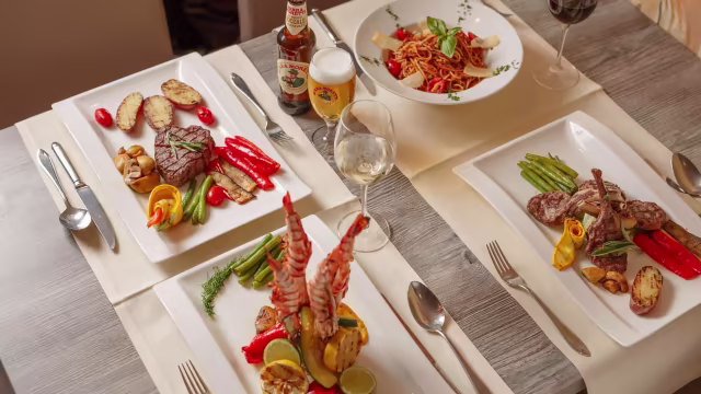Een elegante presentatie van verschillende gerechten: gegrilde garnalen met limoen, kleurrijke paprika's en asperges; een sappige steak met geroosterde aardappelen en een medley van groenten; en spaghetti in rijke tomatensaus met verse basilicum en geraspte kaas.
