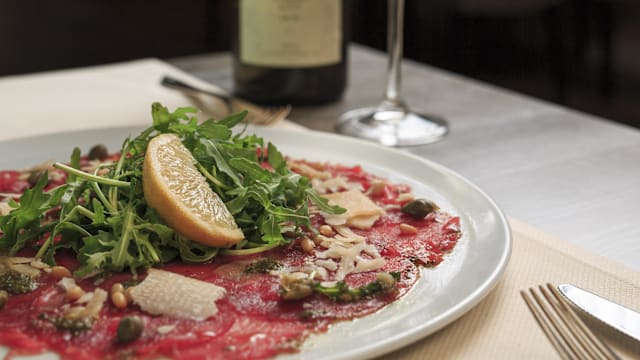Het gerecht bestaat uit dunne plakjes rundvleescarpaccio, gegarneerd met een royale hoeveelheid verse rucola, schijfjes citroen, Parmezaanse kaas en pijnboompitten, met een scheutje pesto voor extra smaak.