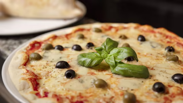 Klassieke pizza met een gouden, krokante korst, rijk tomatensaus, gesmolten kaas, zwarte en groene olijven, en een verse basilicumblaadje.