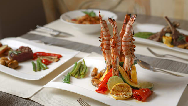 Gegrilde garnalen gepresenteerd op een kleurrijke bed van gebakken groenten, gegarneerd met limoen- en citroenschijfjes en besprenkeld met olijfolie.