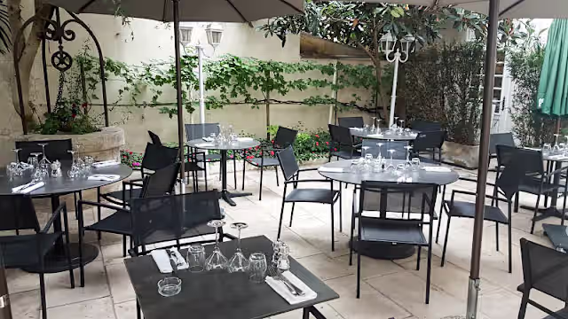Espace de restauration en plein air avec des tables rondes, chaises noires, et une ambiance détendue, agrémenté de verdure luxuriante et d'ombrières.