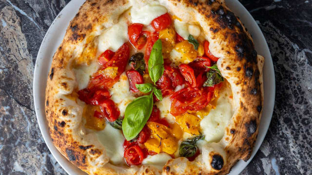 Pizza appena sfornata con crosta dorata e leggermente gommosa, con formaggio fuso, pomodori arrosto e basilico fresco.
