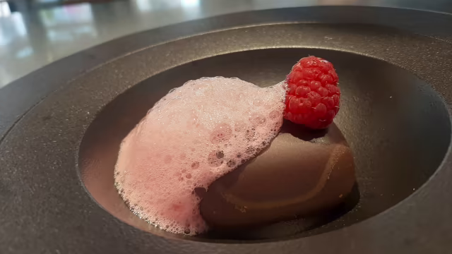 Mousse de chocolate oscuro con espuma de frambuesa y una frambuesa fresca como decoración.