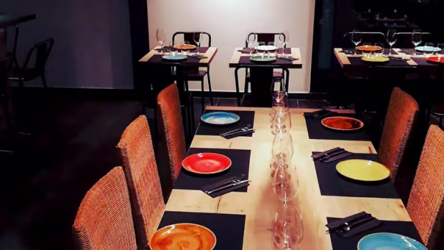 Ambiente acogedor y casual con mesa de madera, sillas de mimbre y vajilla colorida.