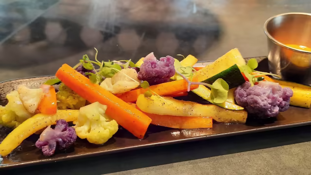 Una colorida mezcla de verduras asadas, incluyendo zanahorias naranjas, calabacín verde y coliflor morada y amarilla, sazonadas ligeramente para resaltar sus colores y texturas.