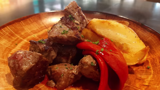 Trozos de carne de res a la parrilla, acompañados de gajos de papa asada y pimiento rojo.