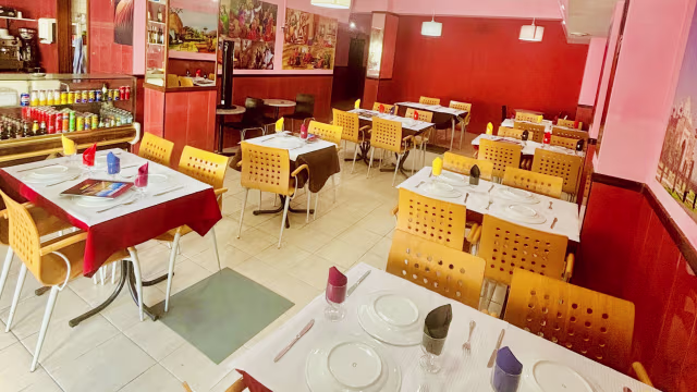 Interior de um restaurante acolhedor com uma atmosfera quente, mesas com toalhas brancas, cadeiras de design moderno e paredes decoradas com arte colorida.