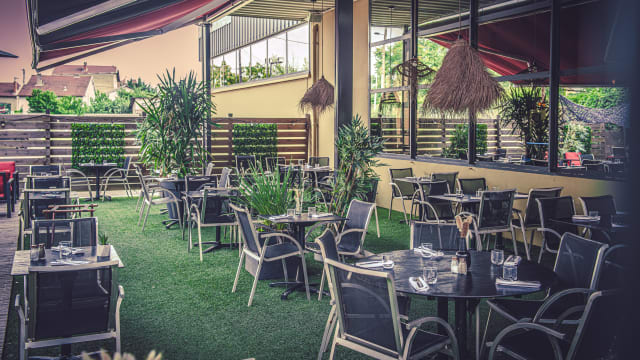 Espace de restauration en plein air avec des tables modernes sur une surface herbeuse, entouré de verdure et de plantes en pot, créant une atmosphère accueillante et relaxante.