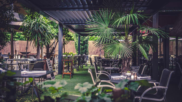 Espace de restauration en plein air spacieux, entouré de verdure luxuriante et de plantes tropicales, avec des tables décorées simplement et des bougies créant une ambiance chaleureuse.