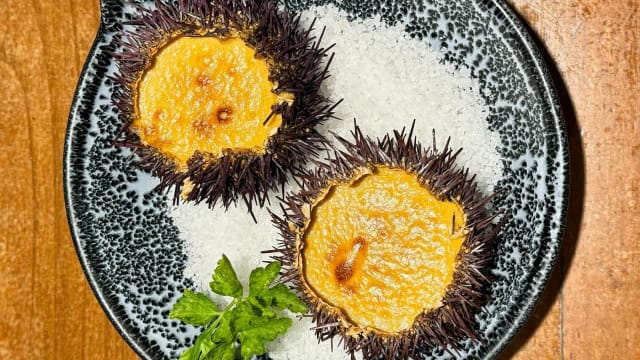 Conchas de erizo de mar rellenas de huevas cremosas, acompañadas de sal gruesa y una ramita de hierba fresca.