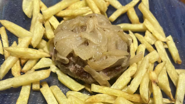 Hamburguesa jugosa con cebollas caramelizadas, acompañada de papas fritas crujientes.
