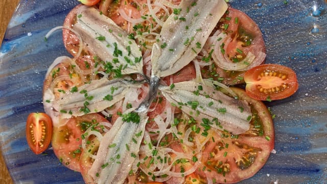 Plato de tomates frescos en rodajas, con anchoas, cebolla en rodajas finas y cebollino picado, acompañado de tomates cherry.