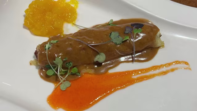 Crepe o pancake relleno con salsa marrón rica, acompañado de una salsa naranja y compota de frutas, decorado con microgreens.
