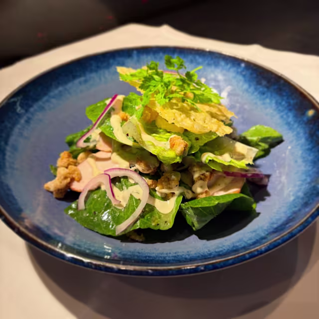 Verse salade met knapperige romaine sla en gemengde groenten, gegarneerd met gesneden gegrilde kip, rode uien en knapperige noten of zaden. Een lichte dressing voegt een romige toets toe aan de presentatie.