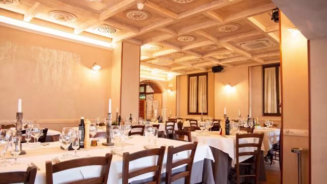 Interno di un ristorante elegante con tavoli apparecchiati, atmosfera calda e accogliente, illuminazione soffusa e dettagli decorativi.