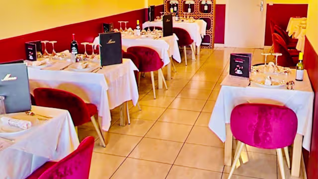 Intérieur du restaurant chaleureux et accueillant, avec des tables élégamment dressées et des chaises en tissu bordeaux, créant une ambiance intime.