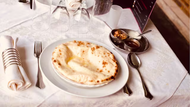 Pain naan fraîchement cuit, moelleux et légèrement grillé, servi chaud avec du beurre fondu, accompagné de sauces chutney et curry.