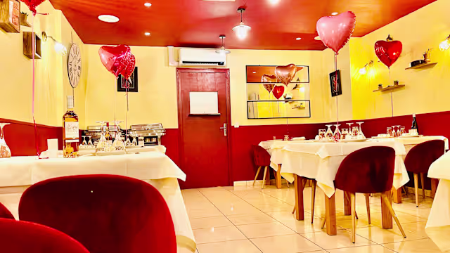 Intérieur chaleureux et accueillant avec des murs jaunes doux et des accents rouges, tables élégamment dressées, chaises en velours bordeaux, et une ambiance romantique.